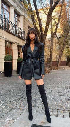 a woman standing on a cobblestone street wearing thigh high boots and a black leather jacket