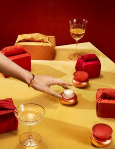 a table topped with red and gold wrapped presents next to wine glasses, candles and boxes