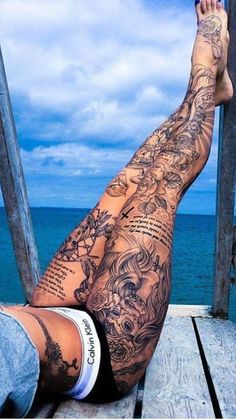 a man with tattoos on his legs is sitting on a dock next to the ocean