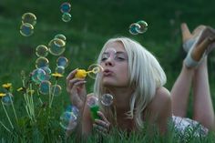 a woman laying in the grass blowing bubbles