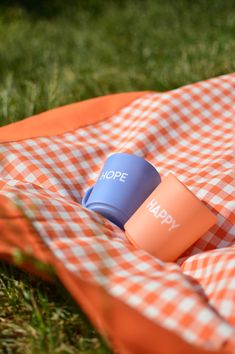 an orange and white checkered blanket on the ground with a coffee cup in it