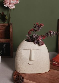 a white vase with flowers in it sitting on a wooden table next to a pine cone