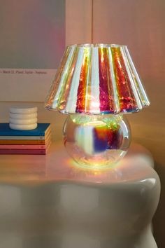 a colorful lamp sitting on top of a table next to a stack of books in front of a window