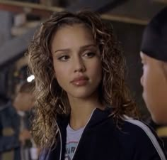 a woman with curly hair is talking to another person in a baseball cap and jacket