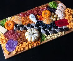 a platter filled with different types of cheeses and fruits on top of a wooden cutting board