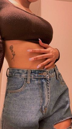 a woman with tattoos on her stomach is wearing ripped jeans and a brown top that has a rose tattooed on the side