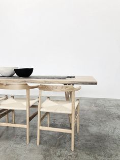 a wooden table with two chairs and a bowl on top of it in front of a white wall