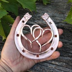 a hand holding a silver brooch with two hearts in it's center, surrounded by leaves