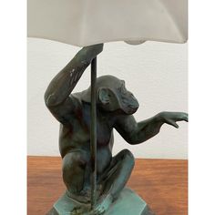 a bronze monkey lamp sitting on top of a wooden table next to a white shade