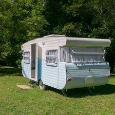 an old blue and white trailer parked on the grass in front of some green trees