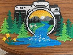 a cross - stitch picture of a camera with water running through the center and mountains in the background