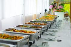 a buffet table with many trays of food and utensils lined up on it