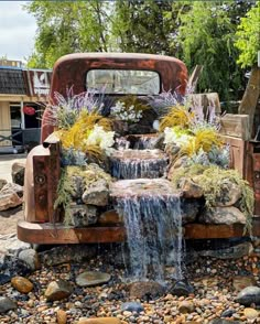 an old truck is decorated with flowers and rocks for a garden waterfall in the back