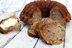 a sliced loaf of banana nut bread next to a cup of yogurt on a white wooden table