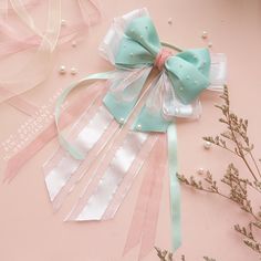 a pink and blue bow with pearls on it next to some ribbons, flowers and beads