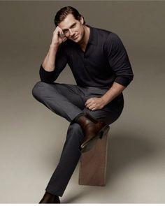 a man sitting on top of a wooden box wearing a black shirt and pants with brown shoes