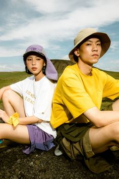 two people sitting on the ground with one person wearing a hat and another in shorts