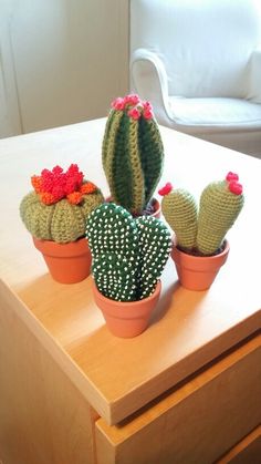 three crocheted cactus plants sitting on top of a wooden table next to a white chair