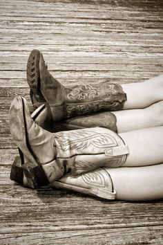 two people with cowboy boots sitting on a wooden floor and one person has their legs crossed