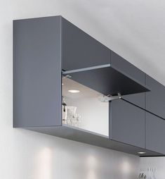 an open cabinet above the sink in a kitchen with wine glasses and utensils