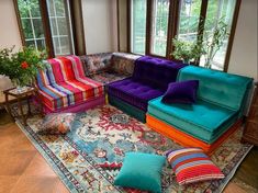 a living room filled with colorful couches and pillows on top of a rug in front of windows