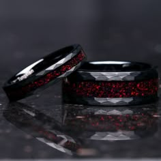 two wedding bands with red glitter inlays on black ceramic, set against a shiny surface