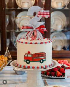 a birthday cake decorated with a firetruck and the number two on top is surrounded by other desserts