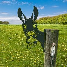 an animal head cut out on the side of a fence post in a field with dandelions