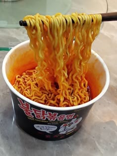 noodles are being lifted from a bucket with chopsticks in it to be eaten