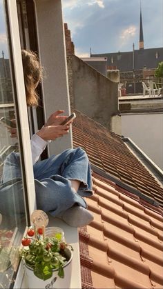 a woman sitting on top of a window sill looking at her cell phone