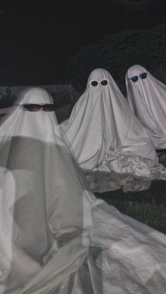 three ghostly people in white cloths sitting on the ground with their heads covered by sheeting