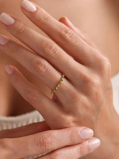 a woman's hand wearing a gold ring with green stones on the middle finger