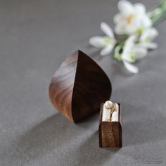 an open wooden ring box sitting on top of a table next to a white flower