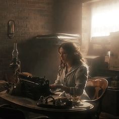 a woman sitting at a table with an old typewriter in front of her and sunlight streaming through the window