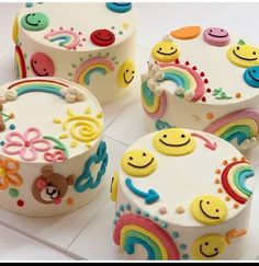 four decorated birthday cakes with smiley faces and rainbows on them sitting on a tray