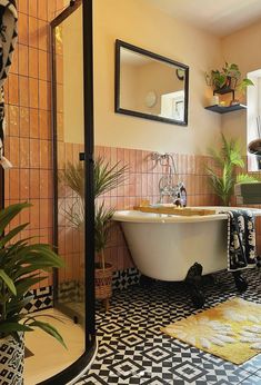 a bath tub sitting inside of a bathroom next to a mirror and potted plants