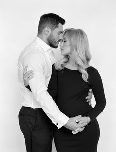 a pregnant couple cuddles in black and white for their portrait session at the studio