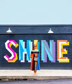 a woman standing in front of a wall with the word shine painted on it