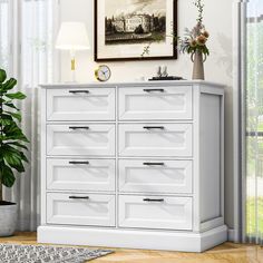 a white dresser with many drawers next to a plant in a vase on the floor