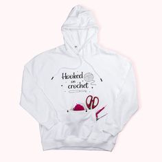 a white hooded sweatshirt with scissors and yarn on the front that says, hooked around