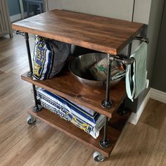 a wooden table with two shelves holding books and bowls on wheels in a living room