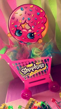 a pink shopping cart filled with lots of candy and donuts on top of a table