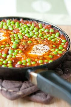 a pan filled with peas and sauce on top of a wooden table next to a spatula