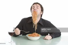 a man sitting at a table eating noodles with a glass of wine in front of him