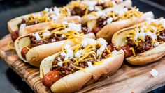 several chili dogs with cheese and onions on a cutting board, ready to be eaten