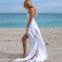 a woman standing on top of a sandy beach next to the ocean wearing a white dress