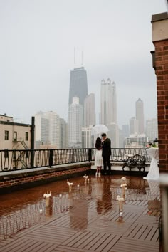 a bride and groom stand under an umbrella on a rainy day in front of the city skyline