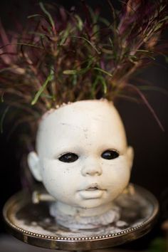 a small white doll head sitting on top of a silver plate with purple flowers in it