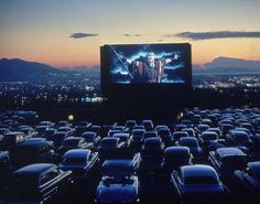 an outdoor movie screen in the middle of a parking lot with cars parked around it