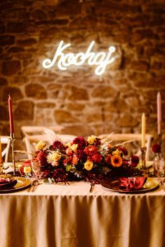 a table topped with plates covered in food next to a stone wall filled with candles and flowers